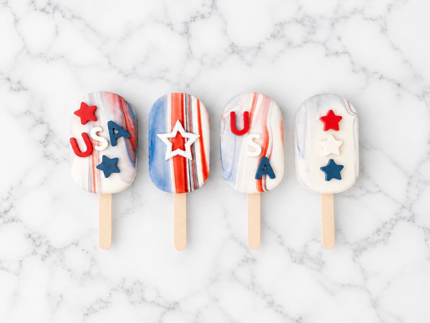 Patriotic popsicle-shaped cake pops decorated with 'USA' lettering, stars, and red-white-and-blue marble drizzle