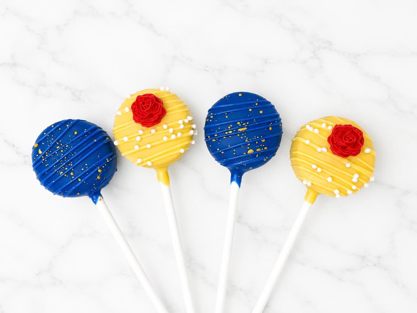 Beauty and the Beast themed cake pops in royal blue with gold flecks and golden yellow with a red rose