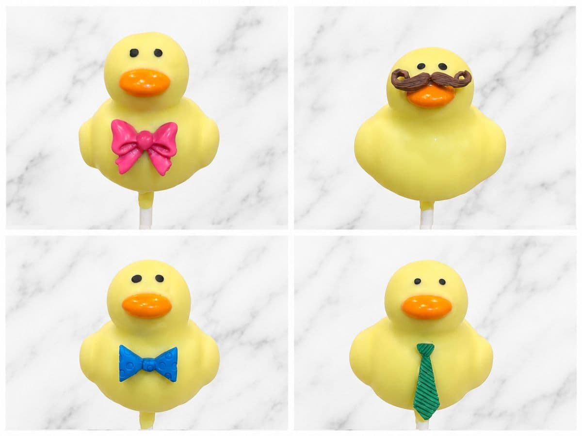 Four rubber-duck-shaped cake pops, each with a different accessory: a pink bow, a mustache, a blue bow tie, and a green necktie