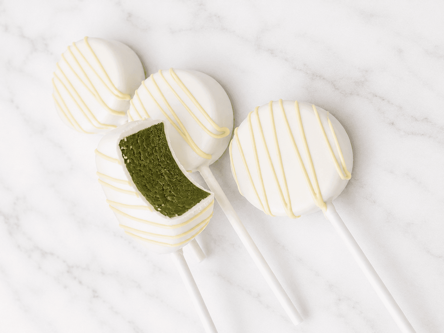 White chocolate cake pops with matcha drizzle, one broken open to show the green matcha cake inside