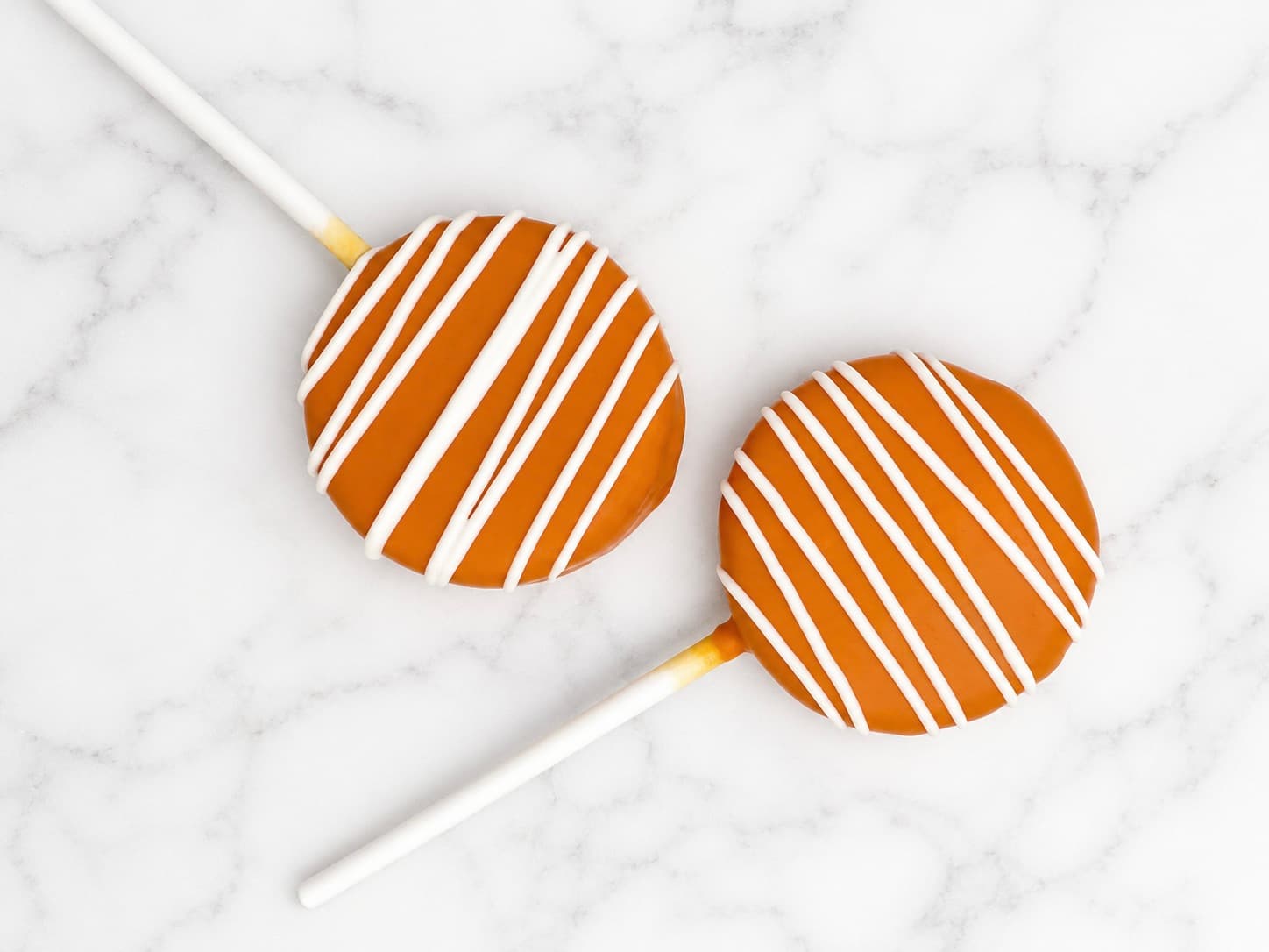 Orange chocolate-dipped cake pops with white drizzle stripes